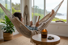 Load image into Gallery viewer, Person reading in hammock with lit candle nearby
